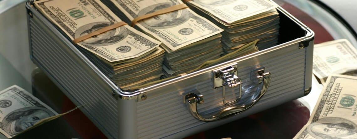 Open briefcase filled with stacks of hundred dollar bills on a glass table, representing wealth.
