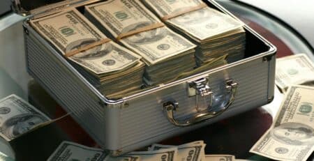 Open briefcase filled with stacks of hundred dollar bills on a glass table, representing wealth.